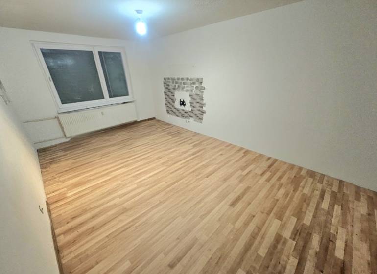 Obývací pokoj s podlahou s dřevěným dekorem a oknem ve 3-pokojovém bytě.