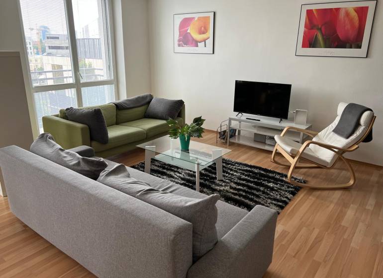 Světlý obývací pokoj s pohovkami, křeslem a televizí v dvoupokojovém bytě.