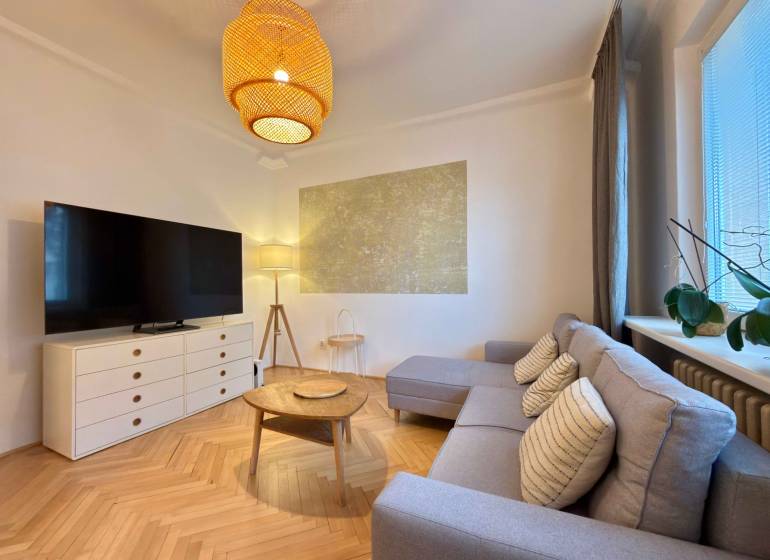 Obývací pokoj v 2-pokojovém bytě s podlahou s dřevěným dekorem, sedačkou a TV.