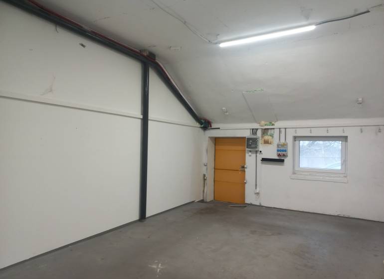 Interiér výrobních prostor s bílými stěnami a oknem s mřížkou.