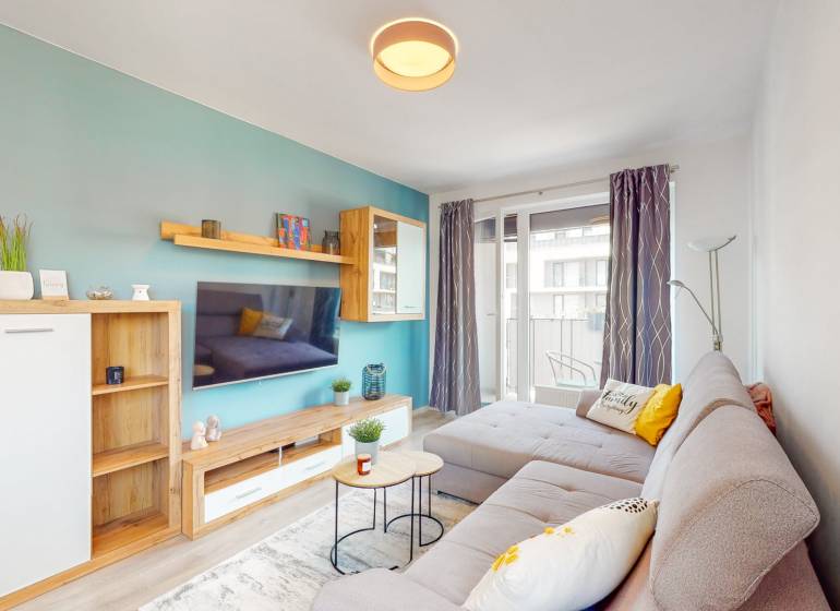 Obývací pokoj v 3-pokojovém bytě s pohodlnou sedačkou a balkonem, podlaha s dřevěným dekorem.