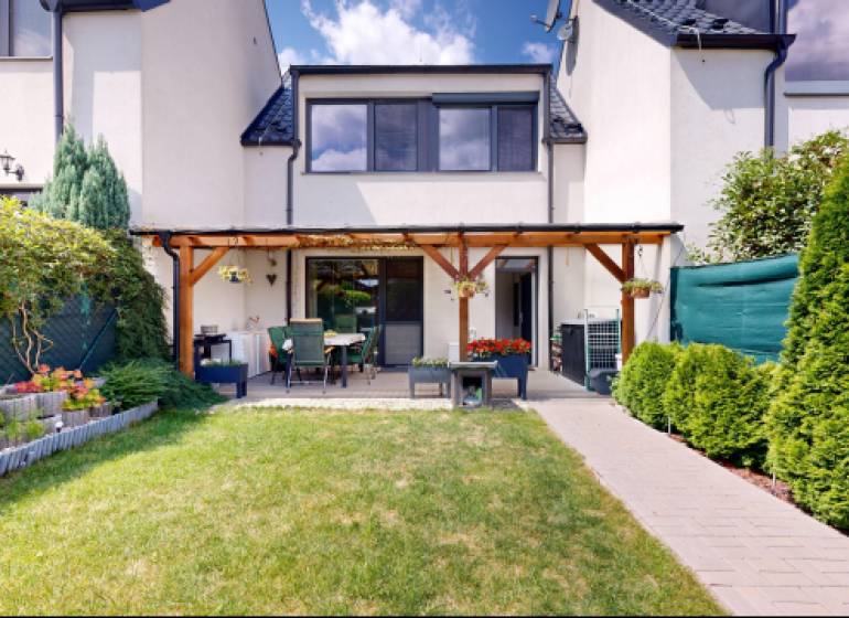 Zahrada a terasa u rodinného domu ve Stupavě s upraveným trávníkem a záhonem.