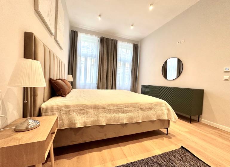 Ložnice v 2-pokojovém bytě s velkou postelí, lampou a podlahou s dřevěným dekorem.