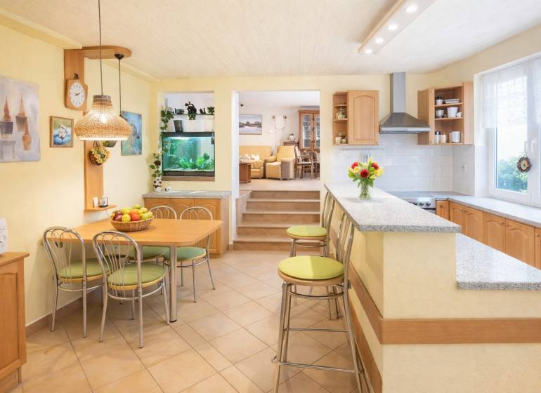 Kuchyně a jídelna s barem v rodinném domě, světlé odstíny a akvárium.