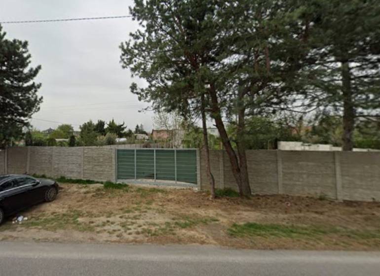 Pozemky - komerční na Dukelské v Bernolákově s betonovým plotem a příjezdovou cestou.