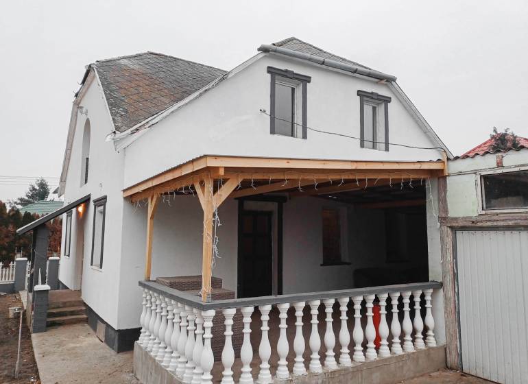 Rodinný dům ve Vizsoly s terasou, bílou fasádou a dřevěným přístřeškem.