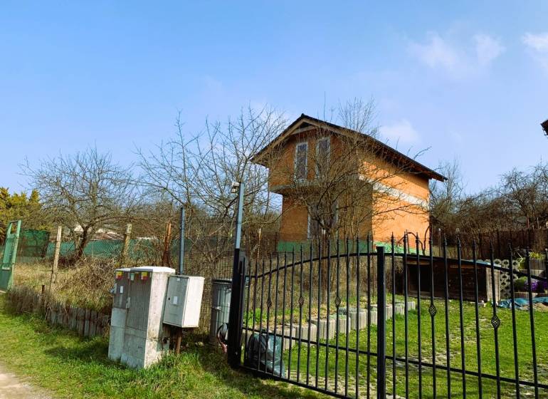 Na obrázku je chata obklopená stromy a plotem na travnatém pozemku.