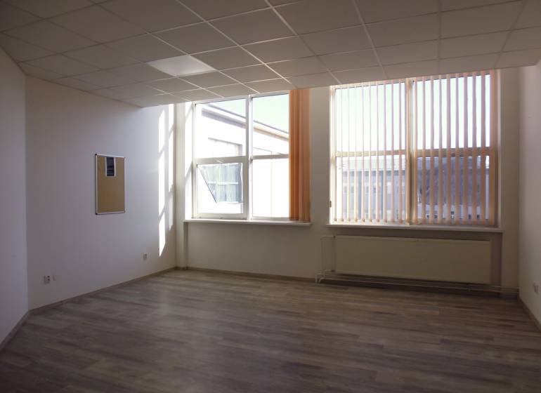 Interiér kanceláře s podlahou s dřevěným dekorem, velká okna a radiátor.