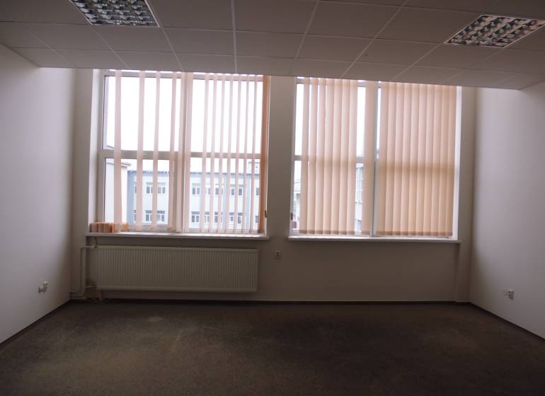 Kancelář s velkým oknem, žaluziemi a podlahou s dřevěným dekorem.