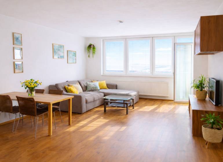 Obývací pokoj v 2-pokojovém bytě s rohovou pohovkou a podlahou s dřevěným dekorem.