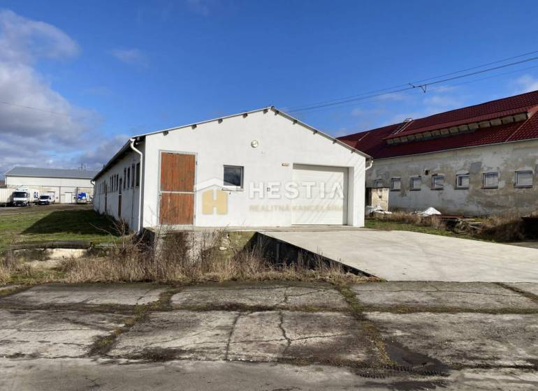 Exteriér skladů a hal v Rybkách s bílou fasádou a dřevěnými dveřmi.