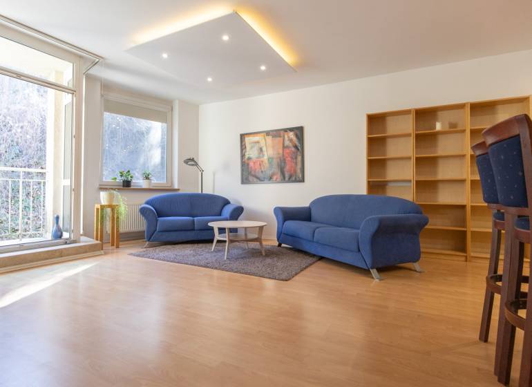 Obývací pokoj v 3pokojovém bytě s modrými sedačkami a podlahou s dřevěným dekorem.