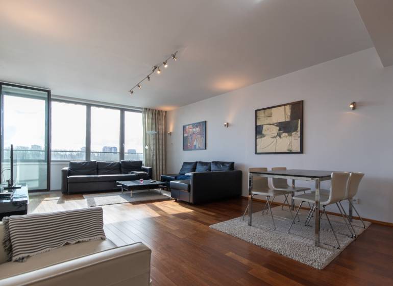 Obývací pokoj s velkými okny, podlaha s dřevěným dekorem, pohodlný nábytek a jídelní kout.