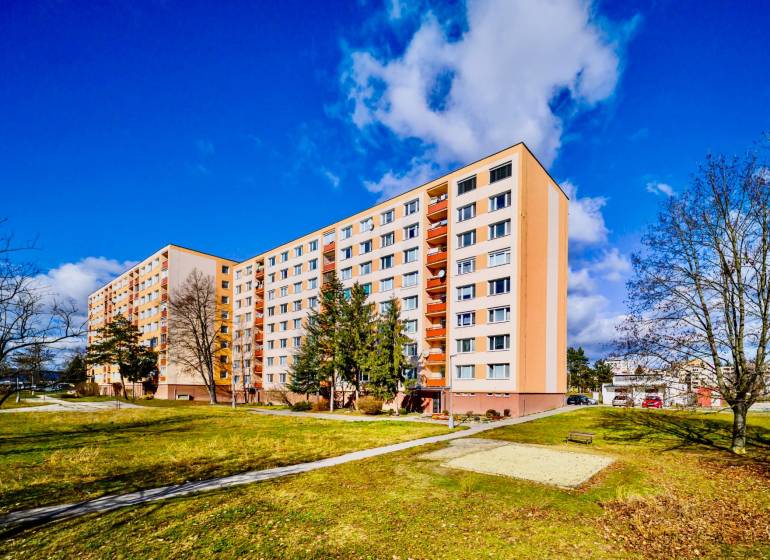 Panelový dům na sídlišti Rúbanisko II v Lučenci obklopený zelení a lavičkami.