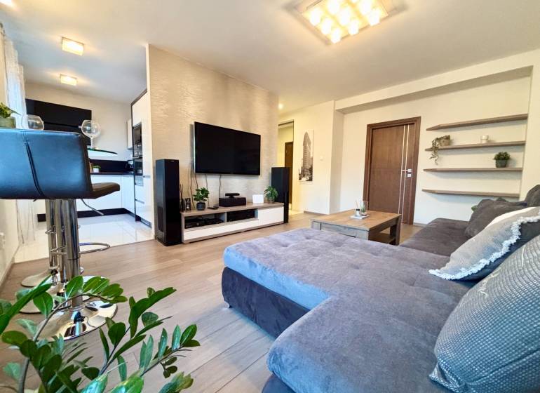 Obývací pokoj v 2-pokojovém bytě s pohodlnou sedačkou a podlahou s dřevěným dekorem.