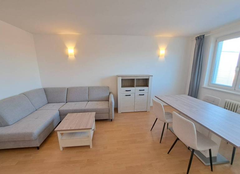 Obývací pokoj ve 4pokojovém bytě s rohovou sedačkou a jídelním stolem.