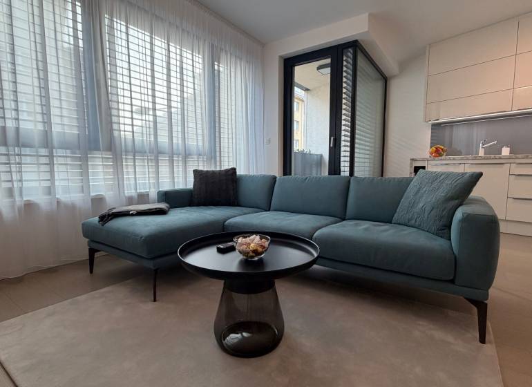 Obývací pokoj s pohovkou, stolkem a kuchyňským koutem v 2-pokojovém bytě.