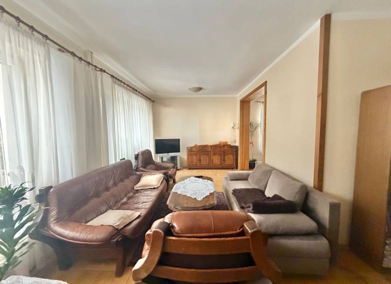 Obývací pokoj v rodinném domě s podlahou s dřevěným dekorem, sedačkou a záclonami.