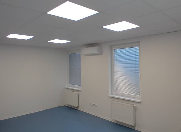 Kanceláře s bílým stropem, modrou podlahou a okny se žaluziemi.