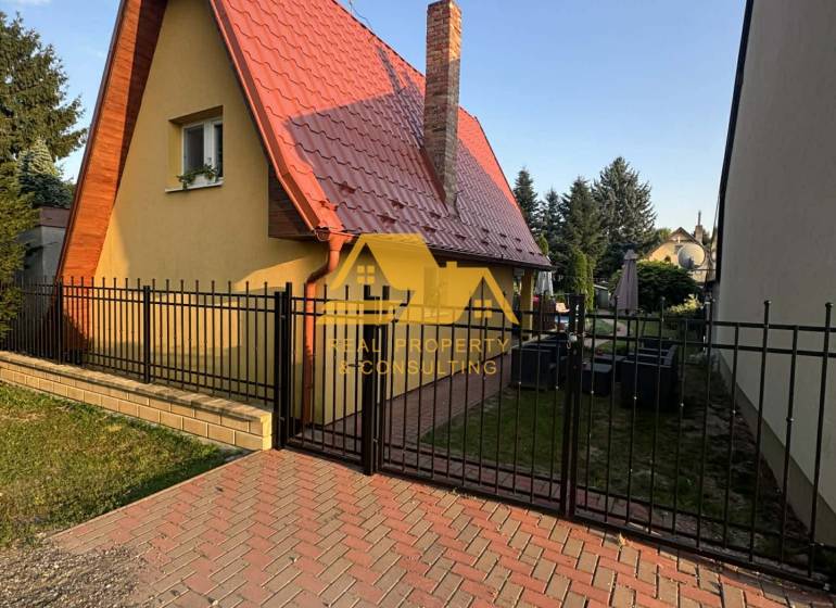 Chata na ulici v Nových Zámcích, se špičatou střechou a cihlovým komínem.