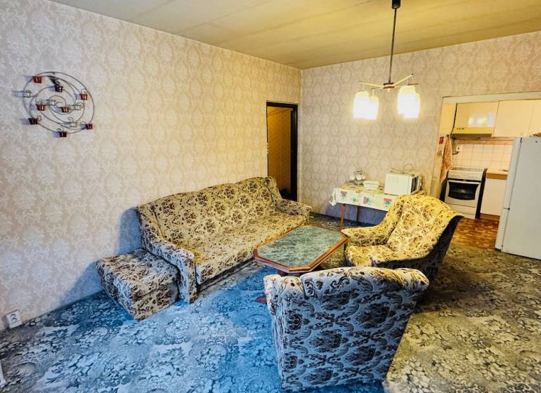 Obývací pokoj s retro sedací soupravou, vzorovaný koberec, vstup do kuchyně v 2-pokojovém bytě.