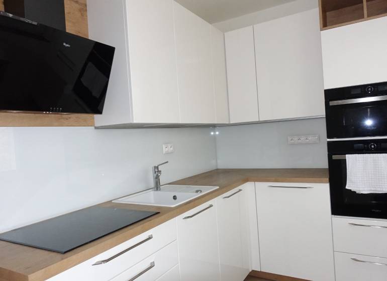 Kuchyně s bílými skříňkami a spotřebiči, doplněná podlahou s dřevěným dekorem v 3pokojovém bytě.