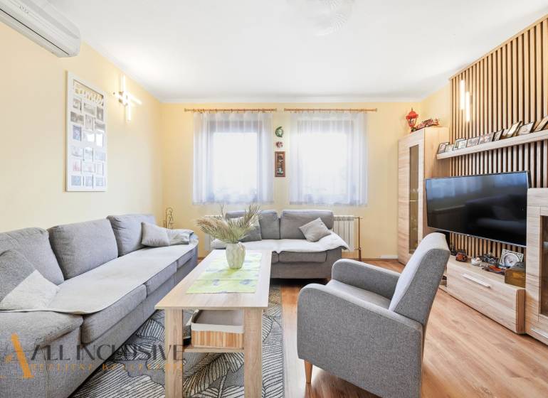 Obývací pokoj v rodinném domě s pohodlnou šedou sedačkou a podlahou s dřevěným dekorem.