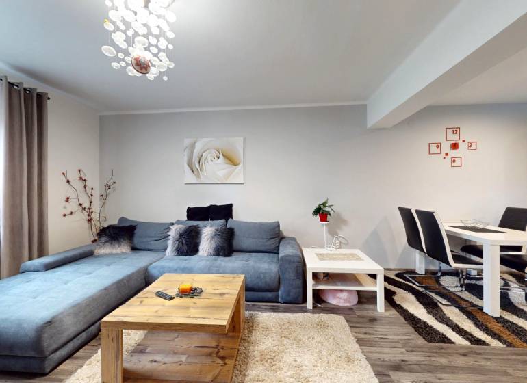 Obývací pokoj v rodinném domě s modrou sedačkou, jídelním stolem a podlahou s dřevěným dekorem.