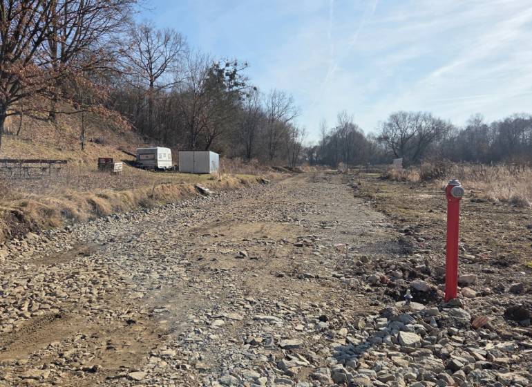 Pozemky - bydlení v Hanisce, kamenitá cesta mezi stromy a kontejner.