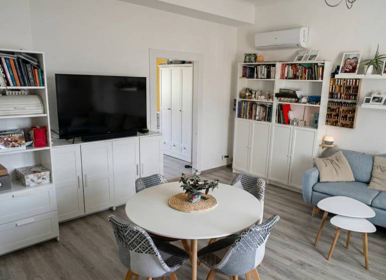 Obývací pokoj v 2pokojovém bytě s podlahou s dřevěným dekorem, gaučem a televizí.