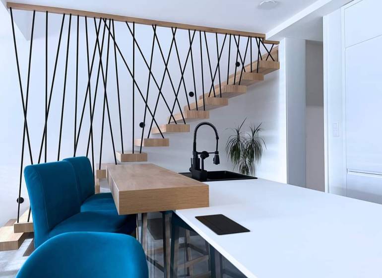 Interiér rodinného domu se schodištěm, modrými židlemi a kuchyňským pultem.