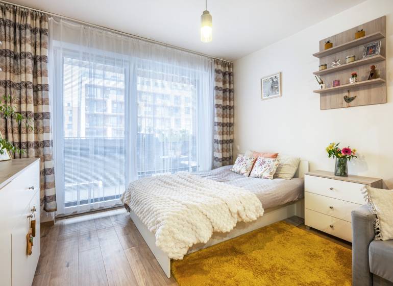 Světlý 1-pokojový byt s postelí, kobercem a podlahou s dřevěným dekorem.