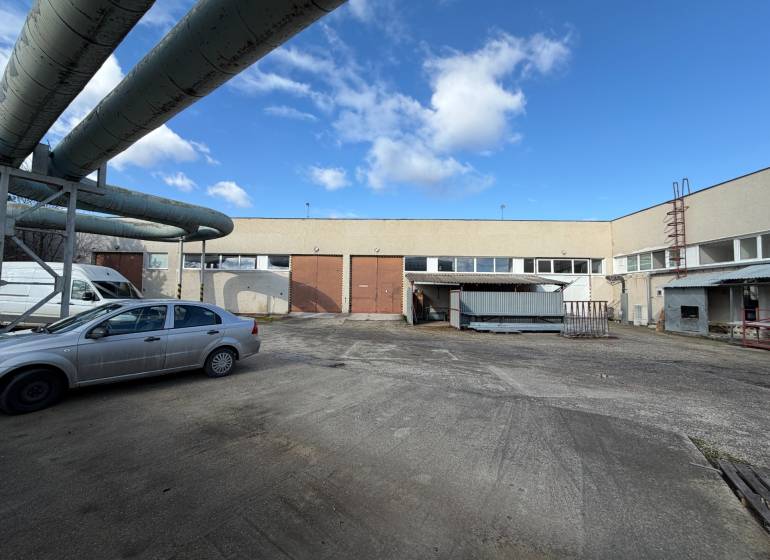 Sklady a haly v Nových Zámcích na ulici Nové Zámky s průmyslovým komplexem a auty.