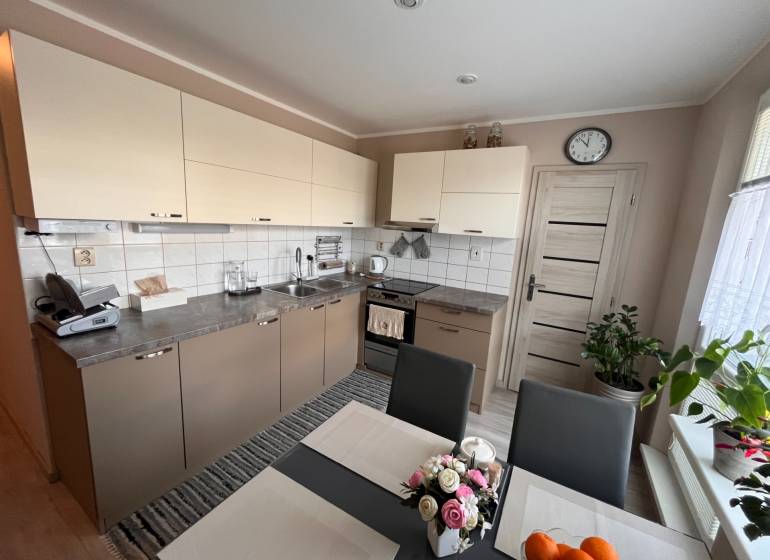 Kuchyně v 3-pokojovém bytě se světlými skříňkami a jídelním stolem.