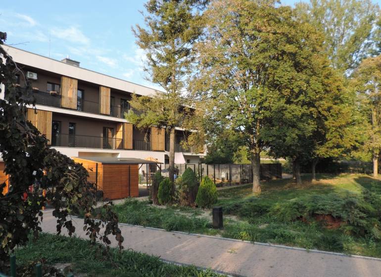 Bytový dům na ulici Bodona, obklopený zelení a stromy, ideální pro bydlení v garsonce.