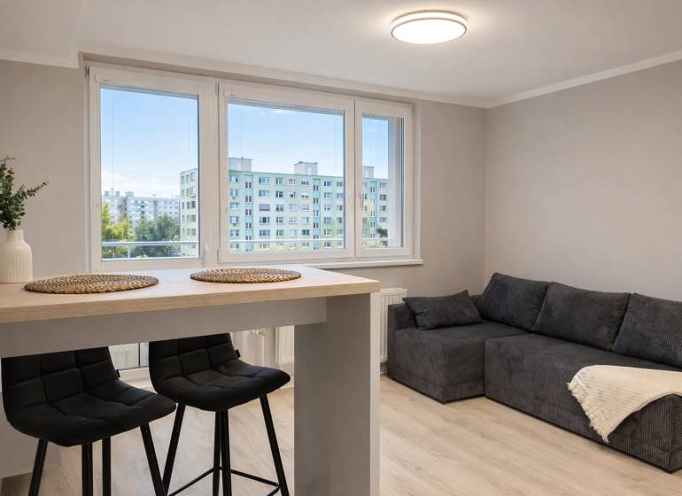 Obývací pokoj v dvoupokojovém bytě s pohovkou, barovým stolem a židlemi.