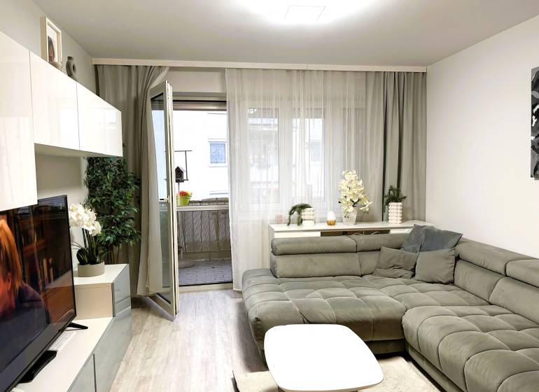 Obývací pokoj v 3-pokojovém bytě s pohodlným sedacím koutem a podlahou s dřevěným dekorem.