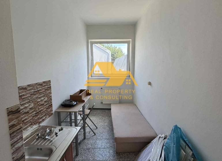 Malá garsonka s umyvadlem, stolem a lehátkem, vhodná pro praktické bydlení.