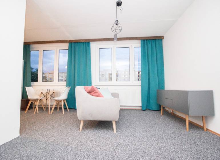 Obývací pokoj ve 4pokojovém bytě s modrými závěsy a šedým nábytkem.