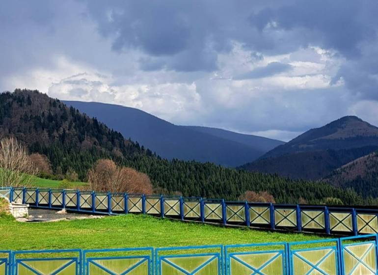 Horské scenérie v Donovalech s modrým dřevěným plotem a lesy v pozadí.