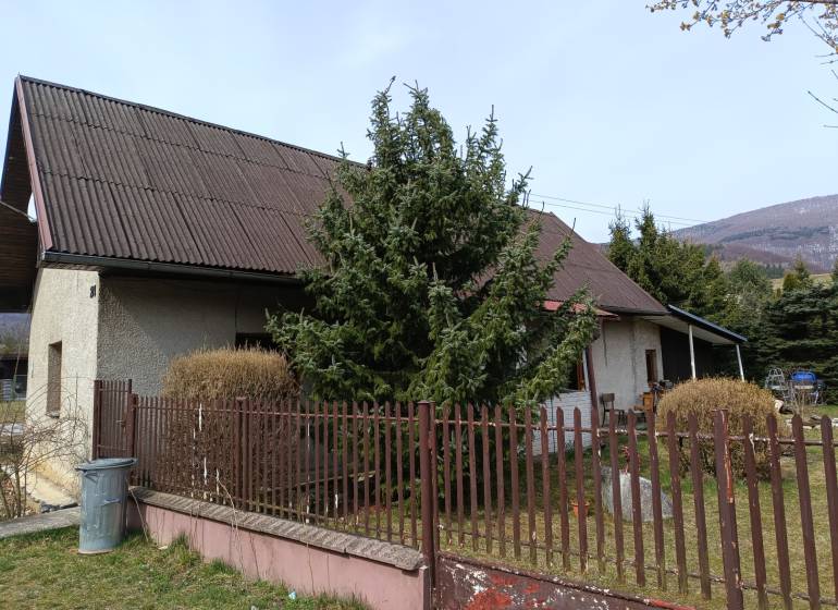 Rodinný dům ve Vrícku s oplocenou zahradou u jehličnatého stromu.