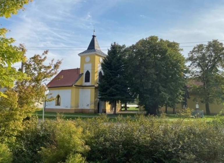 Kostel obklopený zelení v Práznovcích na zemědělských a lesních pozemcích.
