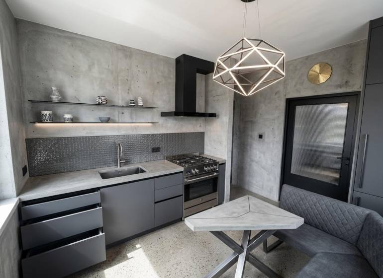Kuchyně v 2-pokojovém bytě s betonovým vzhledem a geometrickým svítidlem.