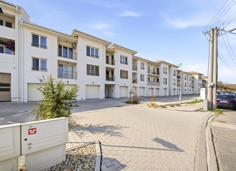 Exteriér 4-pokojového bytu v Dunajské Stredě se světlou fasádou a garážemi.