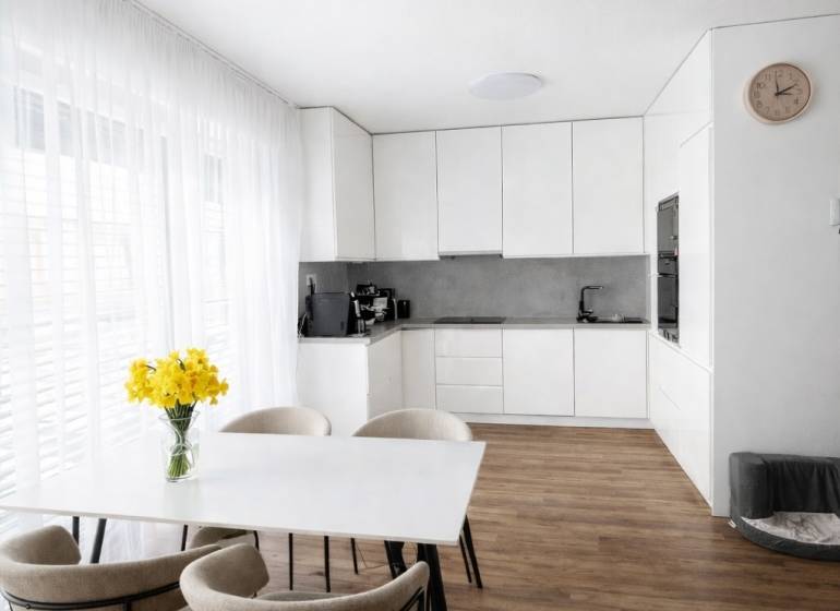 Jídelní stůl se židlemi a kuchyň v 3-pokojovém bytě s podlahou s dřevěným dekorem.