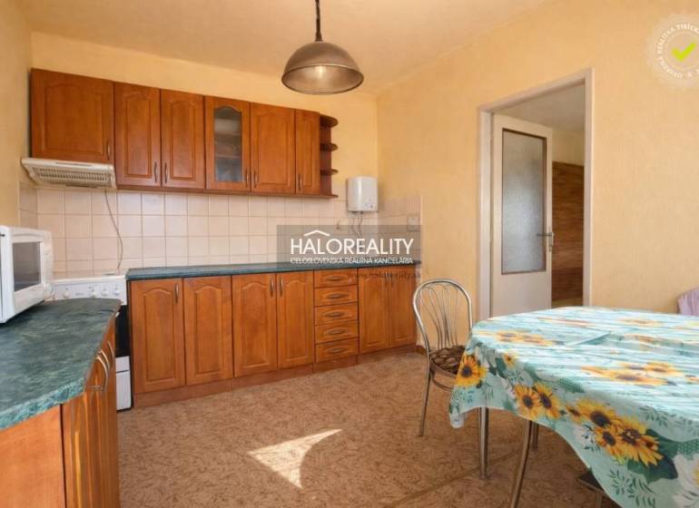 Kuchyně v rodinném domě s vestavěnými skříňkami a stolem s květinovým ubrusem.