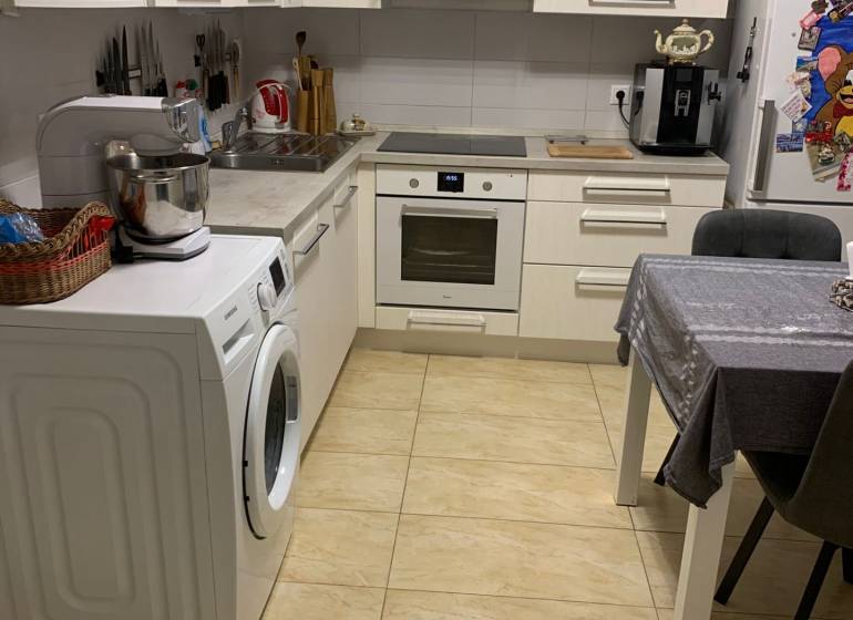 Kuchyně ve 2-pokojovém bytě s bílými skříňkami a keramickou podlahou.