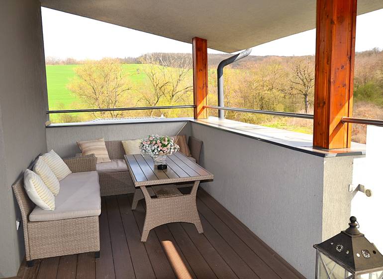 Prostorný balkon s ratanovým nábytkem a podlahou s dřevěným dekorem v garsonce.