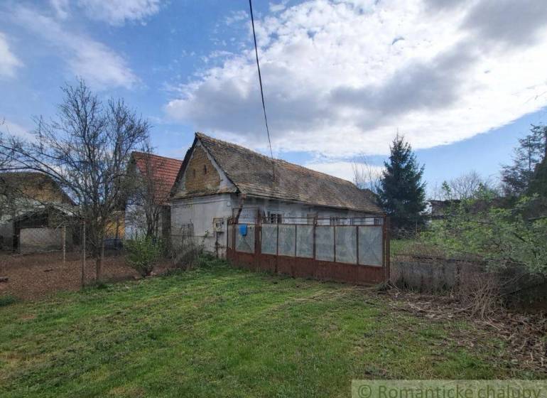 Rodinný dům v Ozdíně, obklopený zahradou a stromy, pod modrou oblohou.