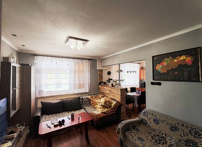 Obývací pokoj s pohovkou, podlahou s dřevěným dekorem a světelným lustrem ve 4pokojovém bytě.